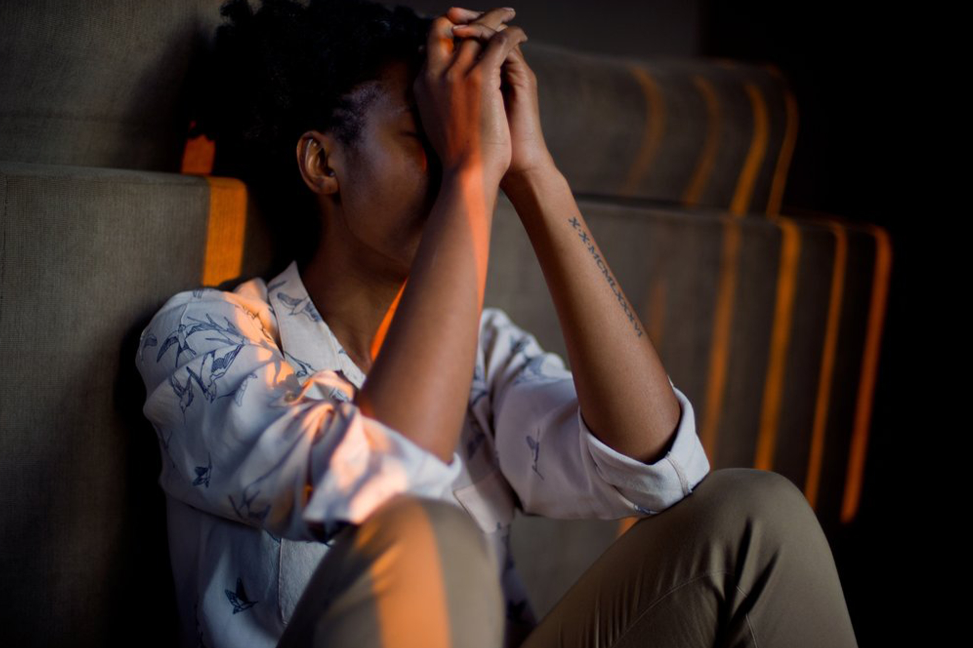 A woman sitting with her elbows resting on her legs and her hands resting against her head.