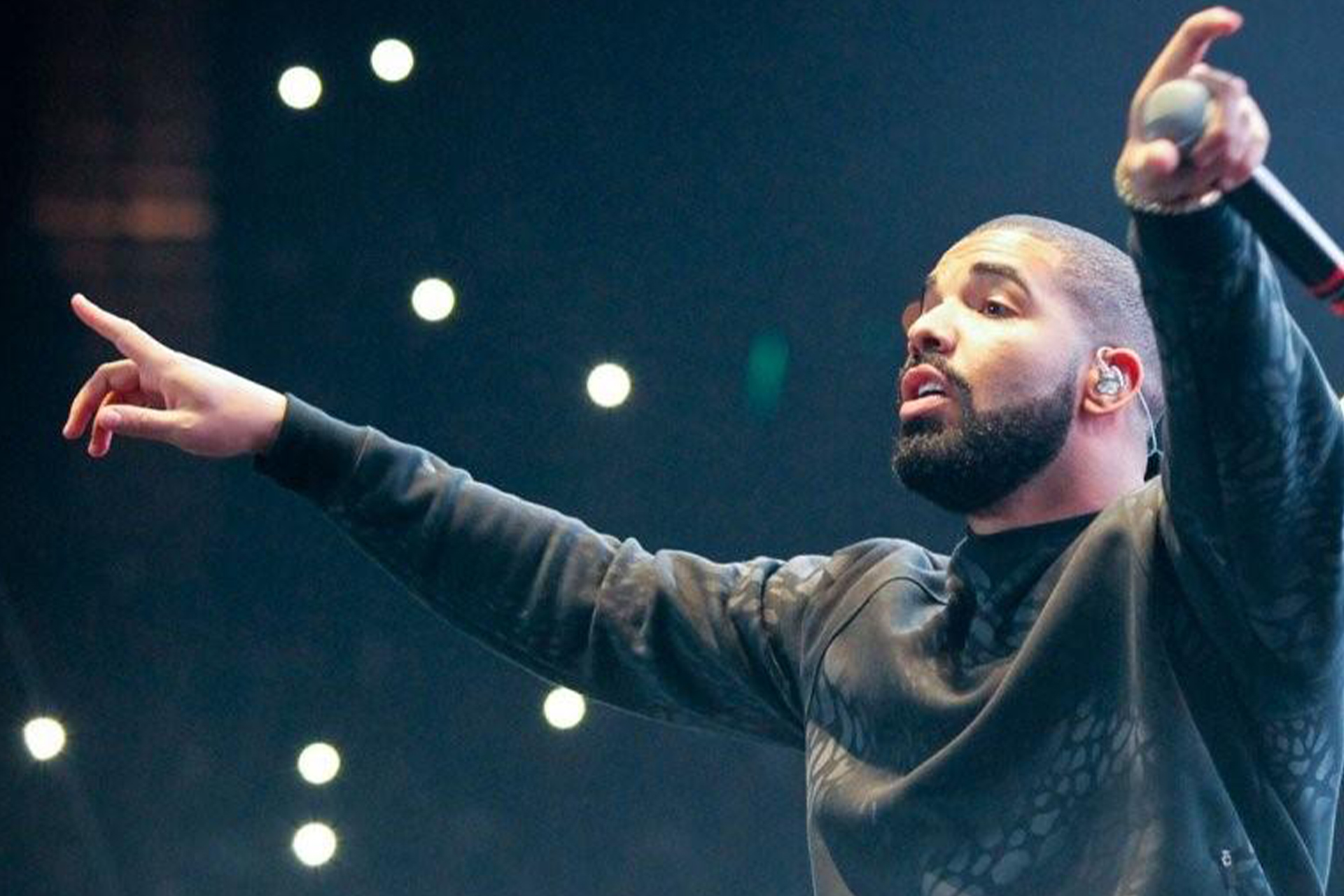 A picture of Drake on stage looking into the crowd with a microphone in his left hand.