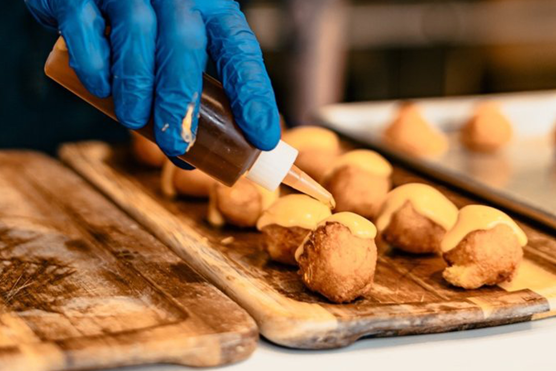 A gloved hand squirting CBD Oil on to round edible treats that are plated on a wooden board.