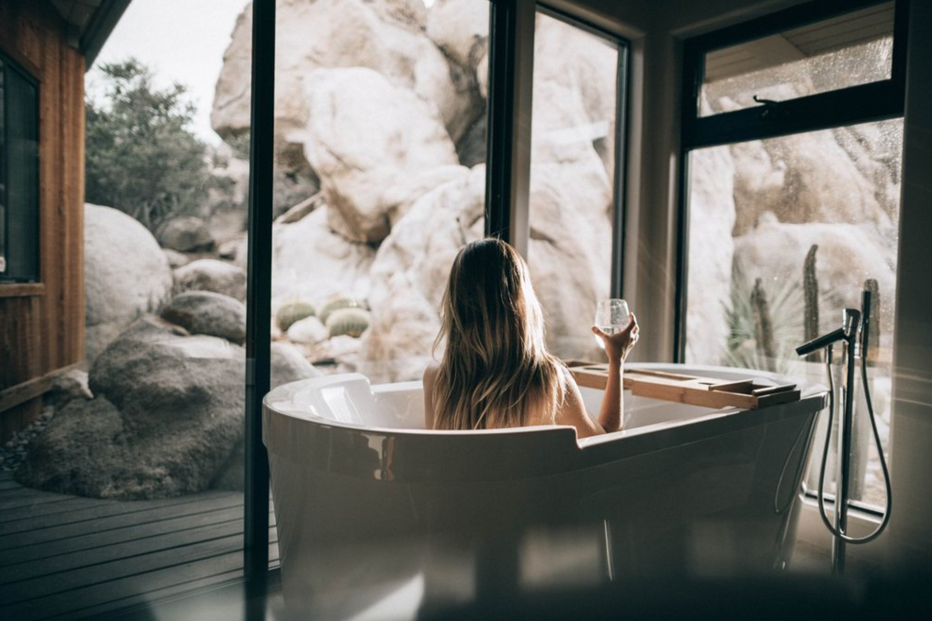 The back of a lady taking a bath, holding a wineglass.