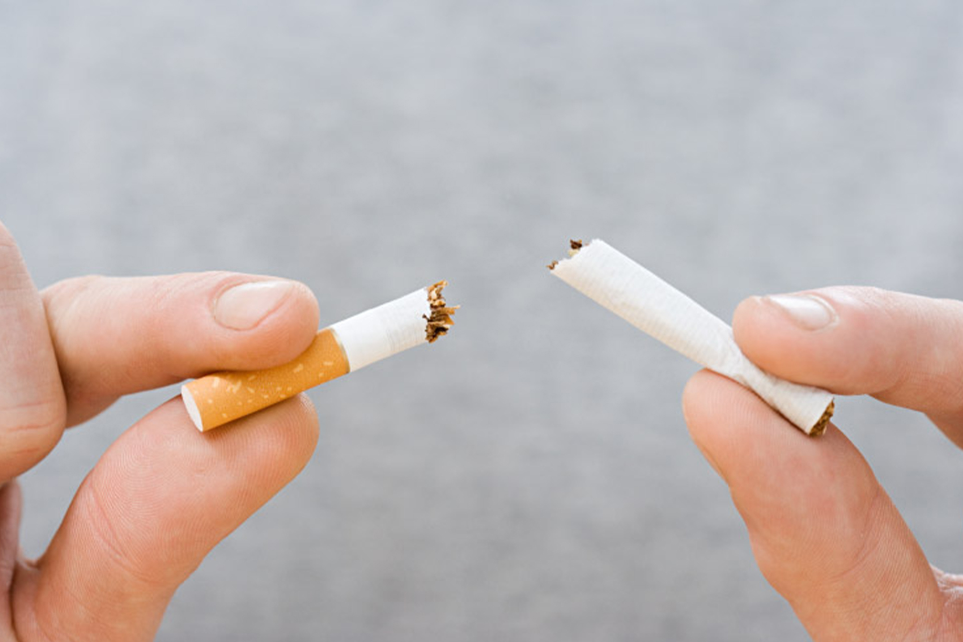 A closeup of two hands breaking a cigarette in two.