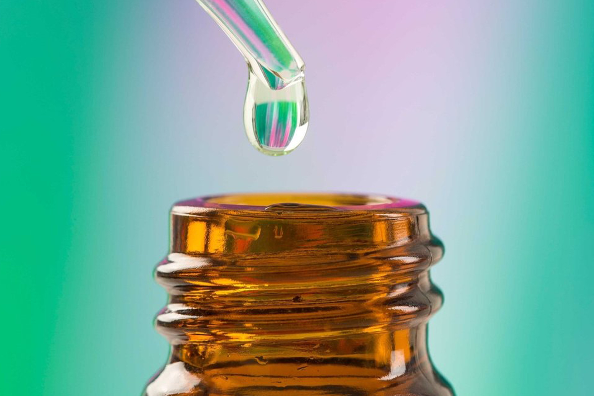 A closeup of a drop of CBD Oil about to drop back into the opening of a glass container.