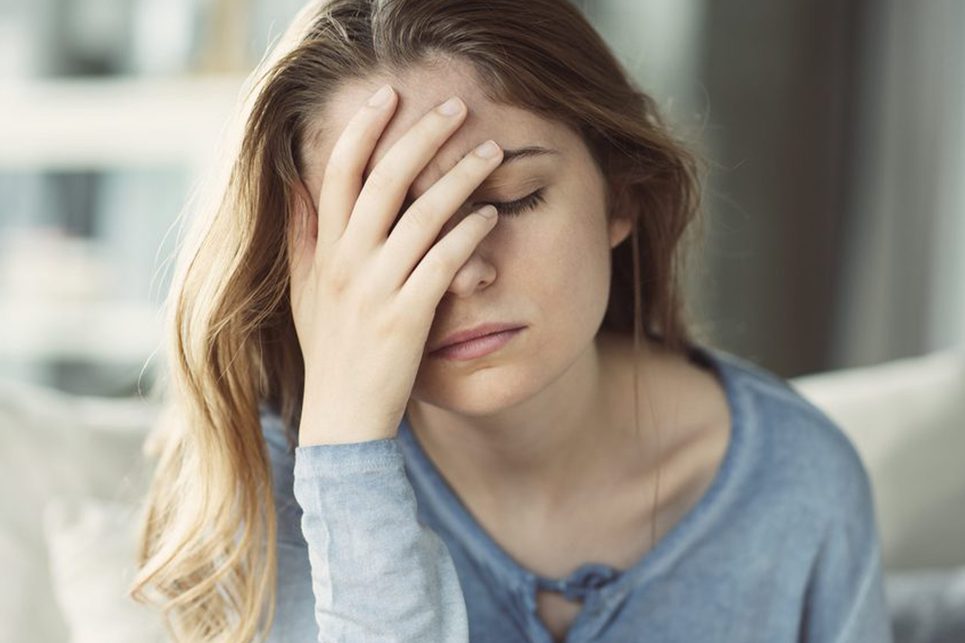 A young lady with a stressed look on her face, holding her head in her left hand, eyes closed.