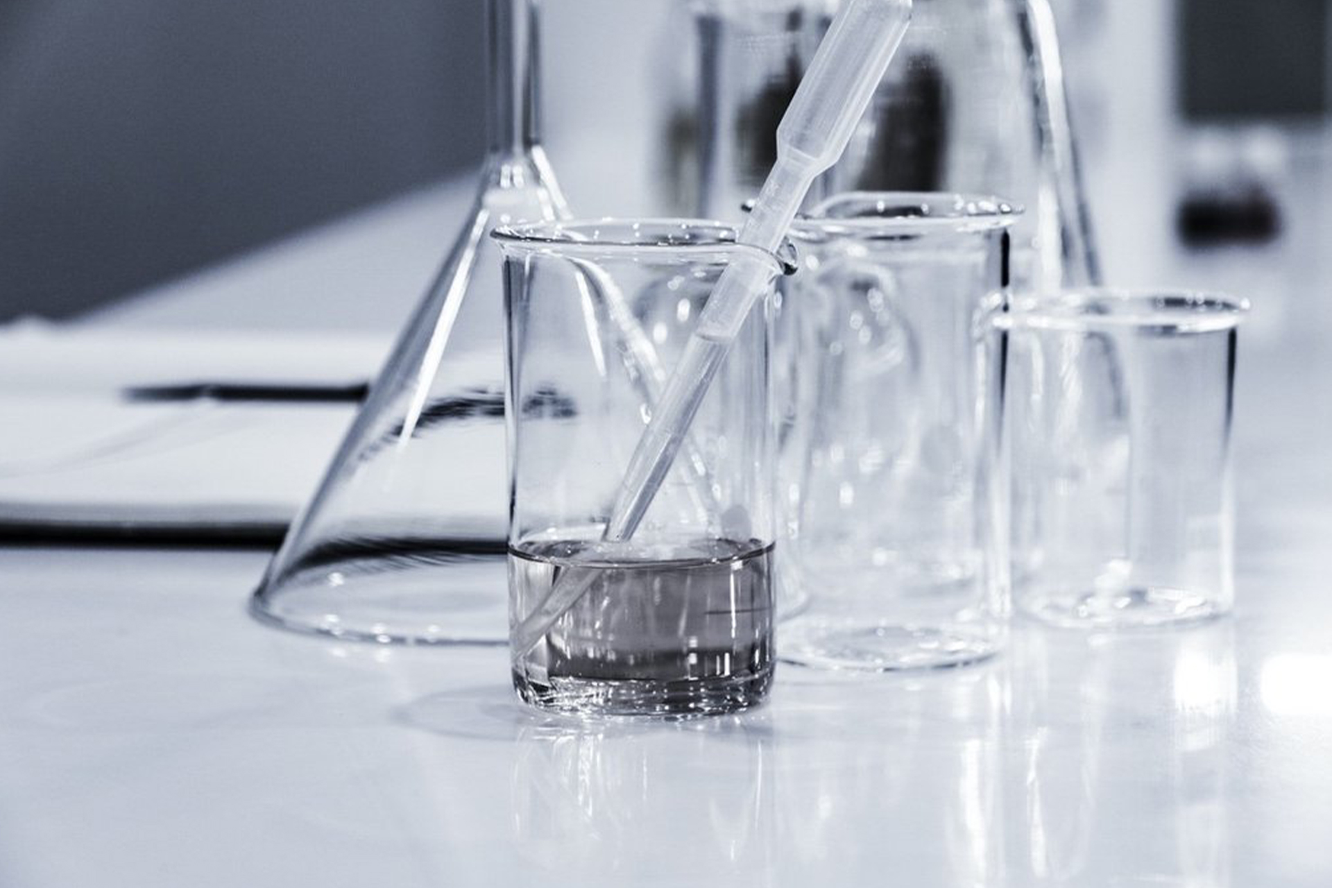 A black and white picture of glass beakers of various sizes, the beaker in front containing some CDB oil as well as an eyedropper.
