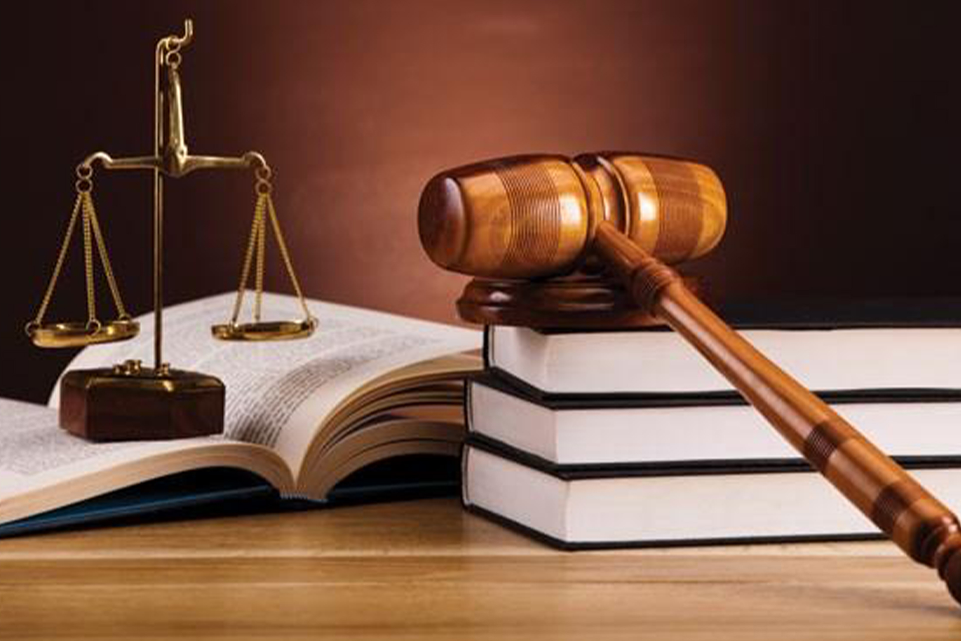 A judge's gavel resting on a stack of books, and a small old-fashioned scale ornament placed on an open book.